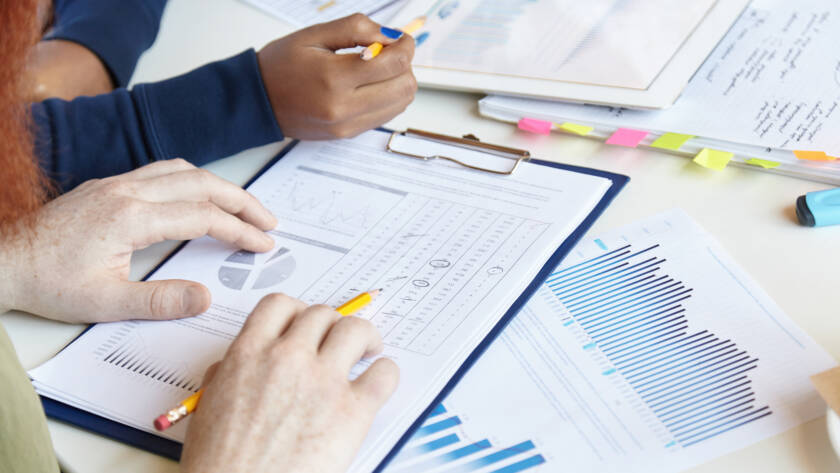 Working in team. Cropped shot of young man holding pencil, studying notes with financial data while sitting at coworking space with his African colleague, discussing business plans and ideas